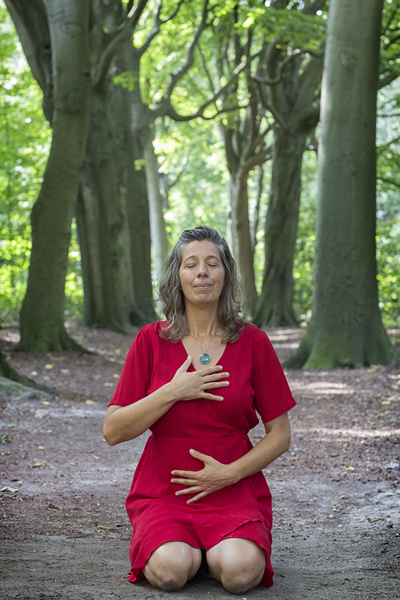 Claudia Heijdel in het bos in seiza zithouding met ogen gesloten en 1 hand op het hart en 1 hand op de buik (Hara)