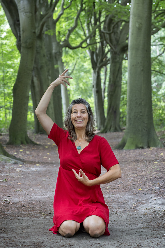Claudia Heijdel in het bos in seiza zithouding met 1 hand bij zonnevlecht en 1 hand boven kruin